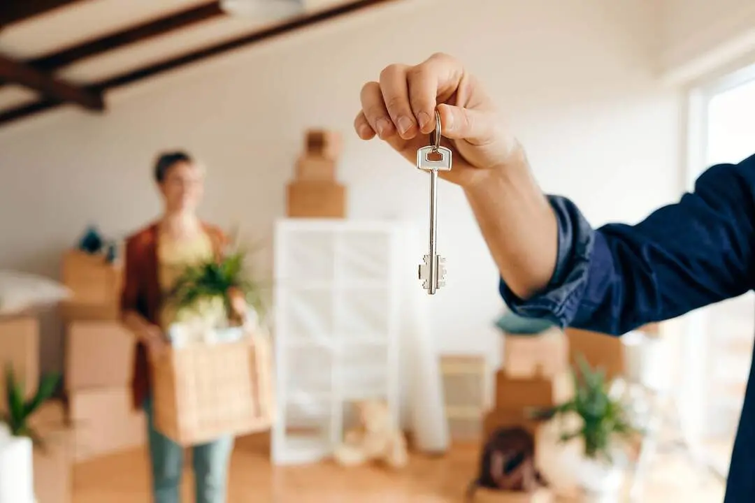 Close-up of a man holding new house key while relocating in a new home with his wife.